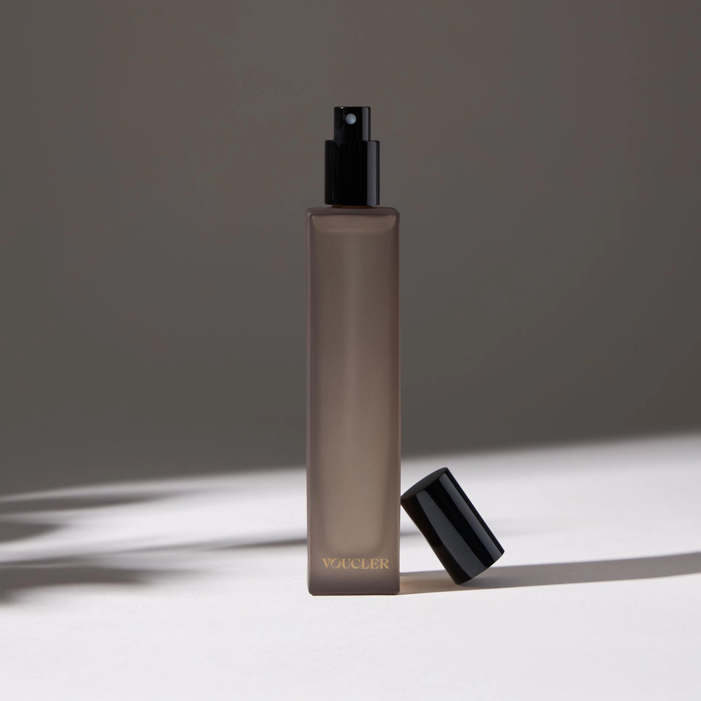 Voucler room spray bottle in dark gray with a black cap next to the bottle, highlighting the minimalist packaging on a neutral background.