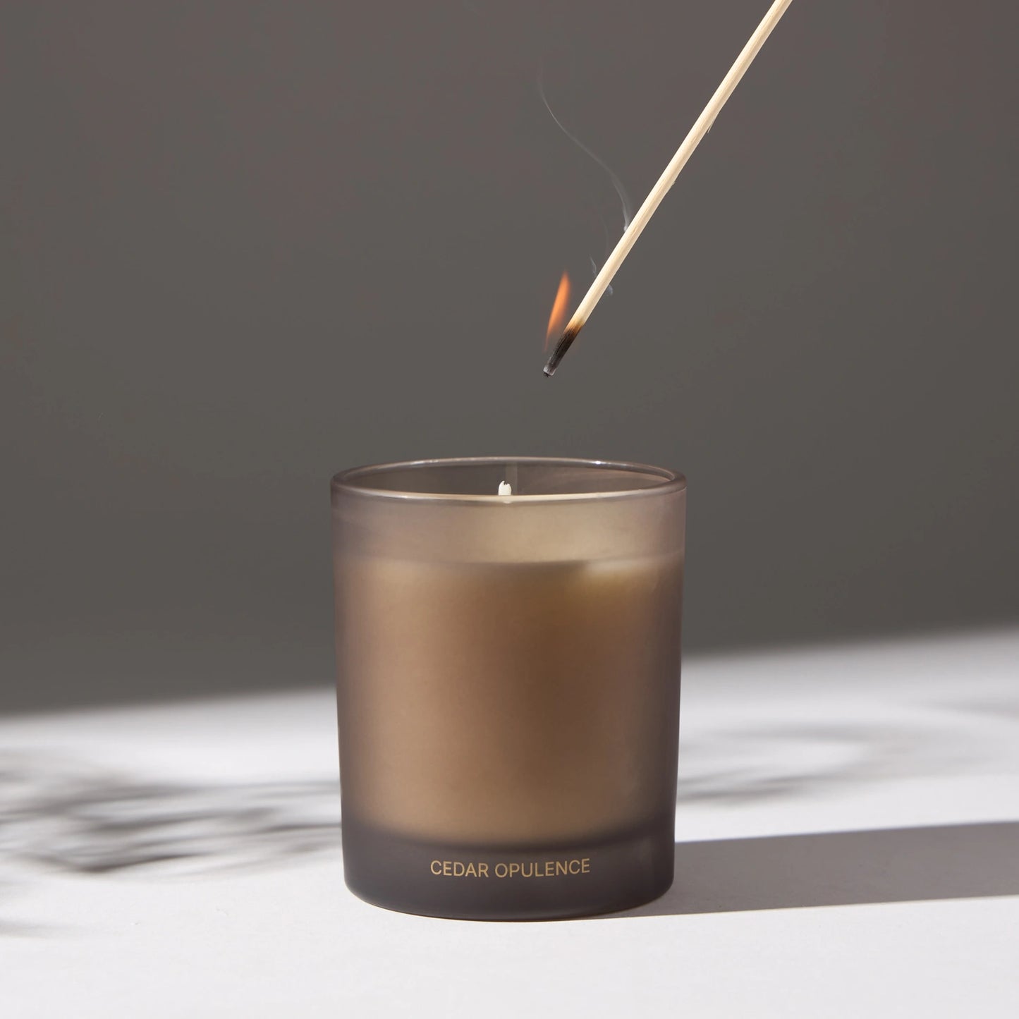 Image of a candle with a lit match being placed on its wick, on a white surface.