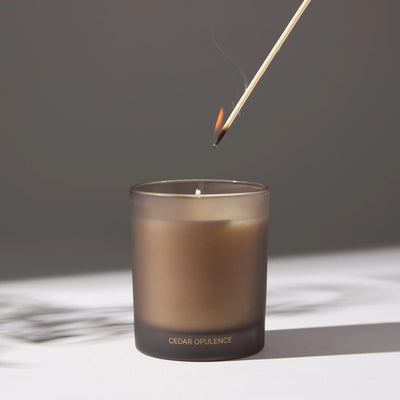 Image of a candle with a lit match being placed on its wick, on a white surface.