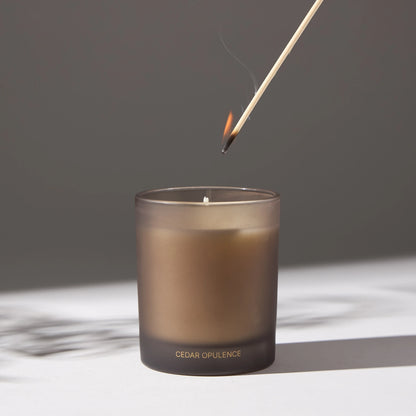 Image of a candle with a lit match being placed on its wick, on a white surface.