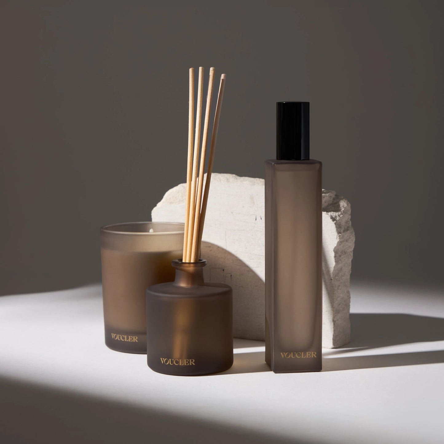 Set of decorative items and air fresheners from the Voucler brand, including a candle, aroma diffuser and spray, with a minimalist background and soft lighting.