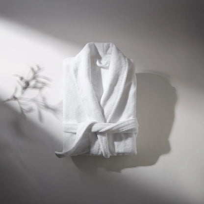 White bathrobe made of soft fabric, placed on a light surface with soft shadow, creating an atmosphere of comfort and relaxation.