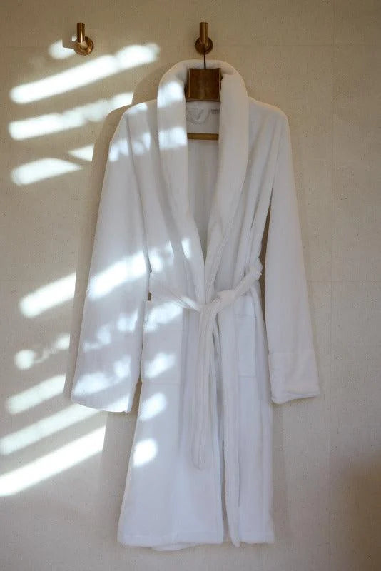 Elegant white bathrobe hanging on the wall with natural light illuminating the room, ideal for moments of relaxation and comfort at home.