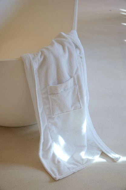 White robe hanging over a white bathtub with a light wood floor.