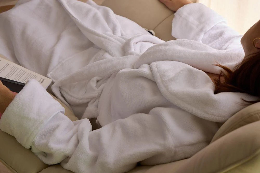 
Woman resting on a sofa, wearing a white bathrobe, in a comfortable and cozy environment.