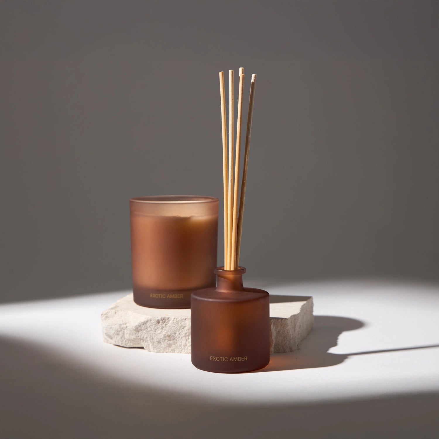 Aroma diffuser with wooden reeds in a brown bottle and candle, decorative and ideal for ambiance with soft fragrances, creating a relaxing atmosphere.