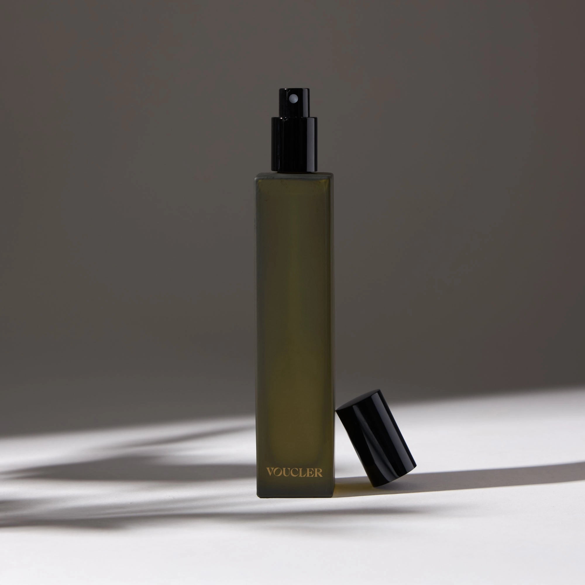 Voucler room spray bottle in dark green with a black cap next to the bottle, highlighting the minimalist packaging on a neutral background.