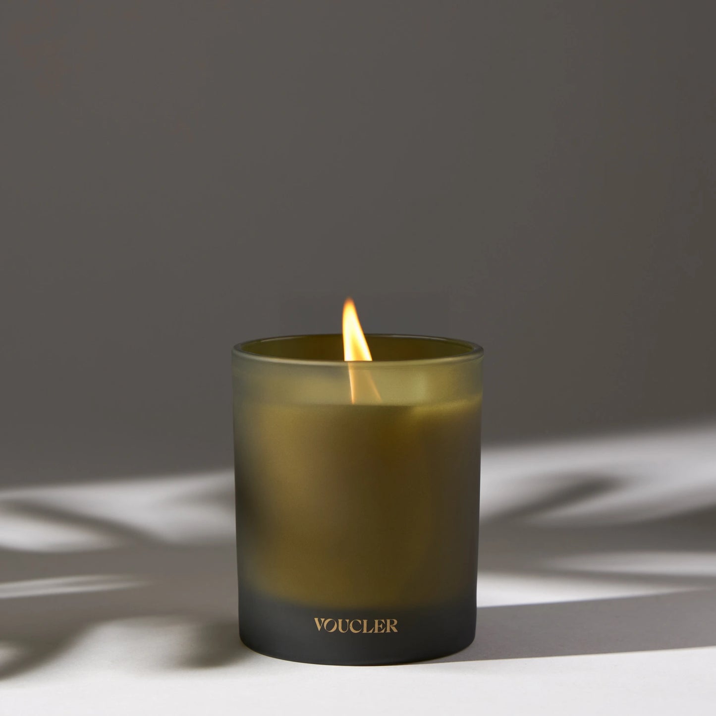 A lit candle on a table casting a soft shadow, creating a warm and inviting atmosphere.