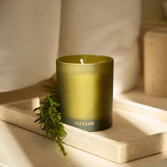 A candle placed on a tray next to a soft towel and a green branch, enhancing a calming and cozy setting.