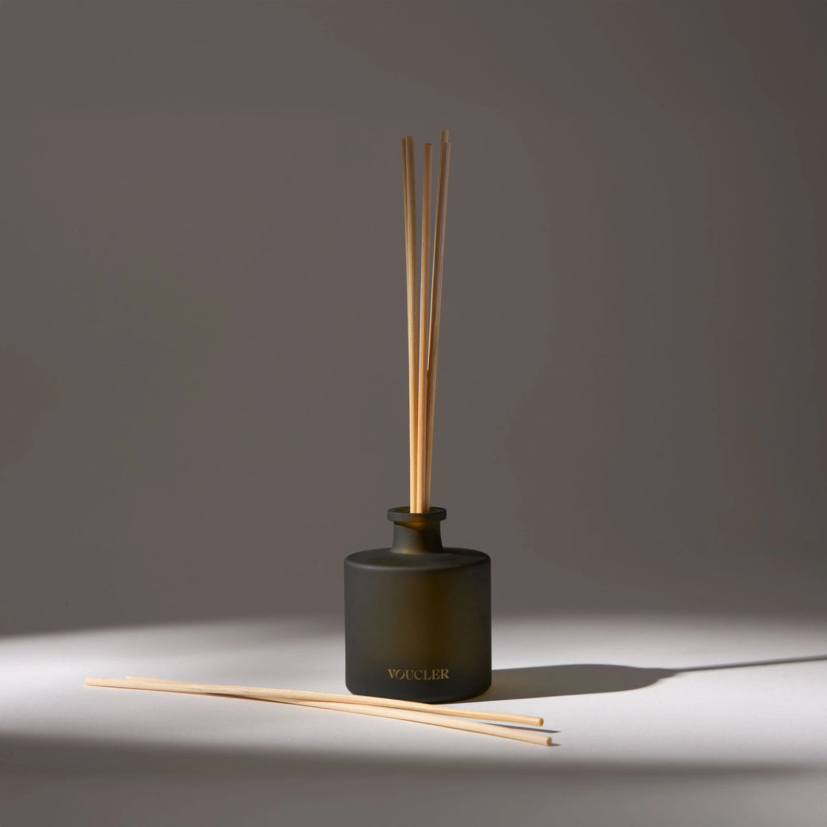 Black glass vase with the name 'Voucler' written on the front, containing several aroma diffuser sticks, placed on a white surface with a drop shadow.