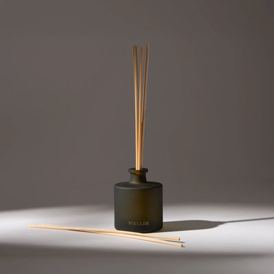 Black glass vase with the name 'Voucler' written on the front, containing several aroma diffuser sticks, placed on a white surface with a drop shadow.
