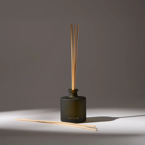 Black glass vase with the name 'Voucler' written on the front, containing several aroma diffuser sticks, placed on a white surface with a drop shadow.