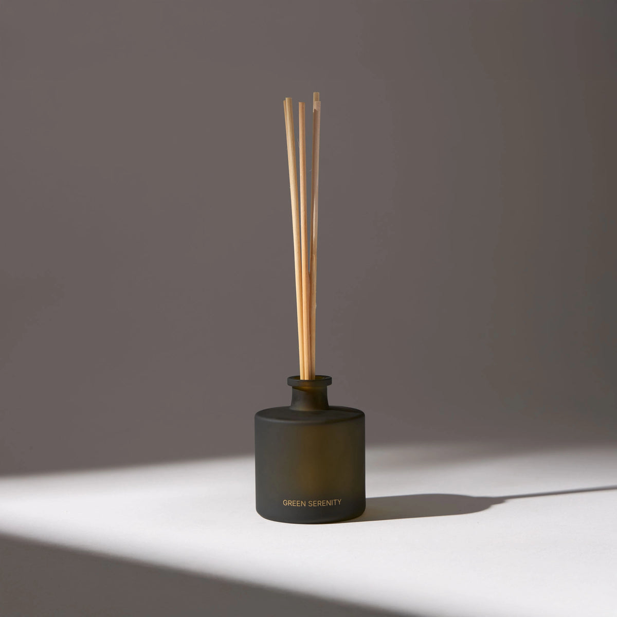 Black glass vase with the name 'Green Serenity' written on the front, containing several aroma diffuser sticks, placed on a white surface with a drop shadow.