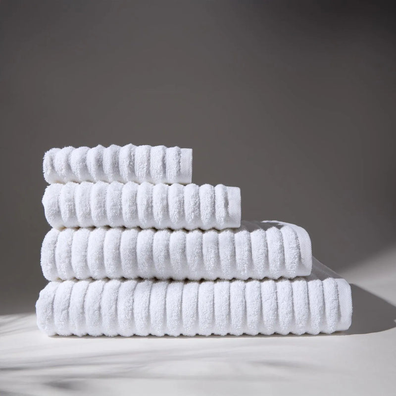 Image of four withe soft towels stacked on top of each other, with a soft gray background, conveying a feeling of cleanliness and care for hygiene.