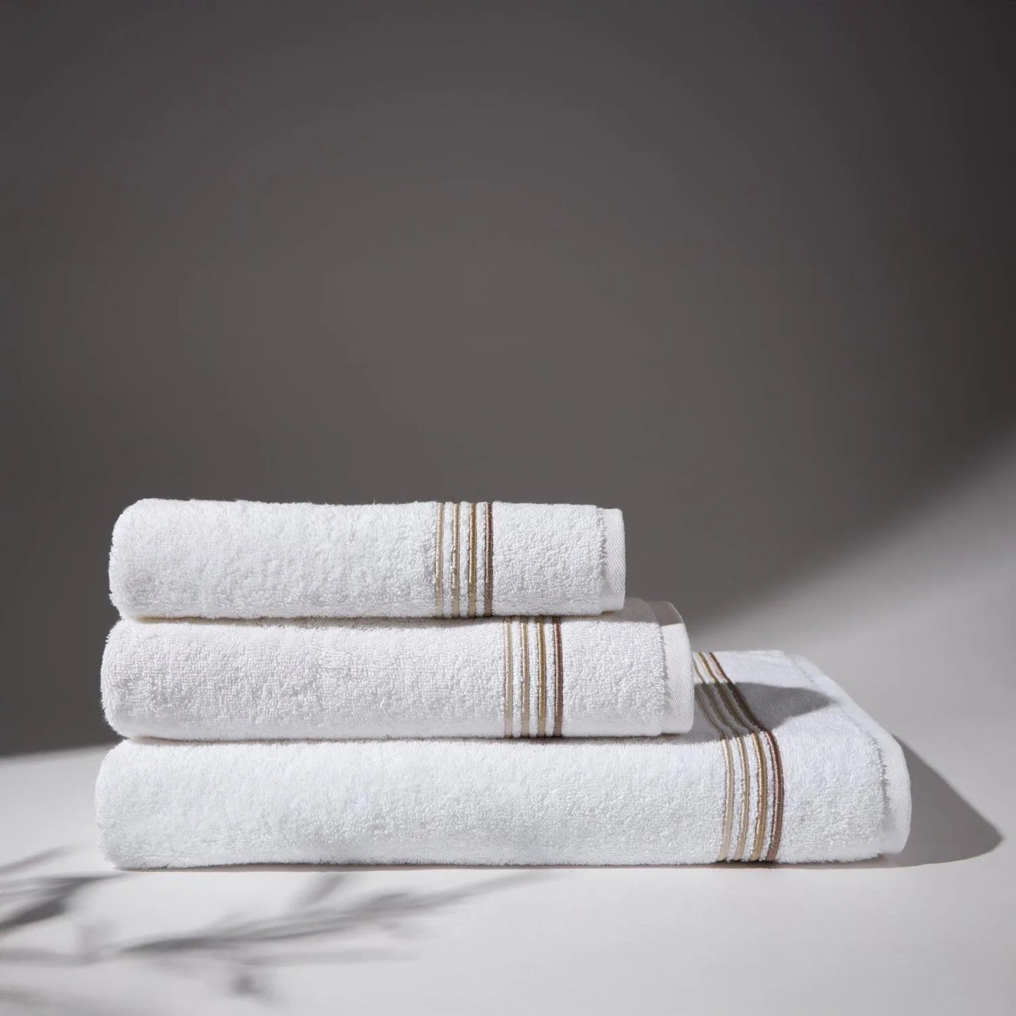 Image of thre beige towels stacked on top of each other, with a soft gray background, conveying a feeling of cleanliness and care for hygiene.