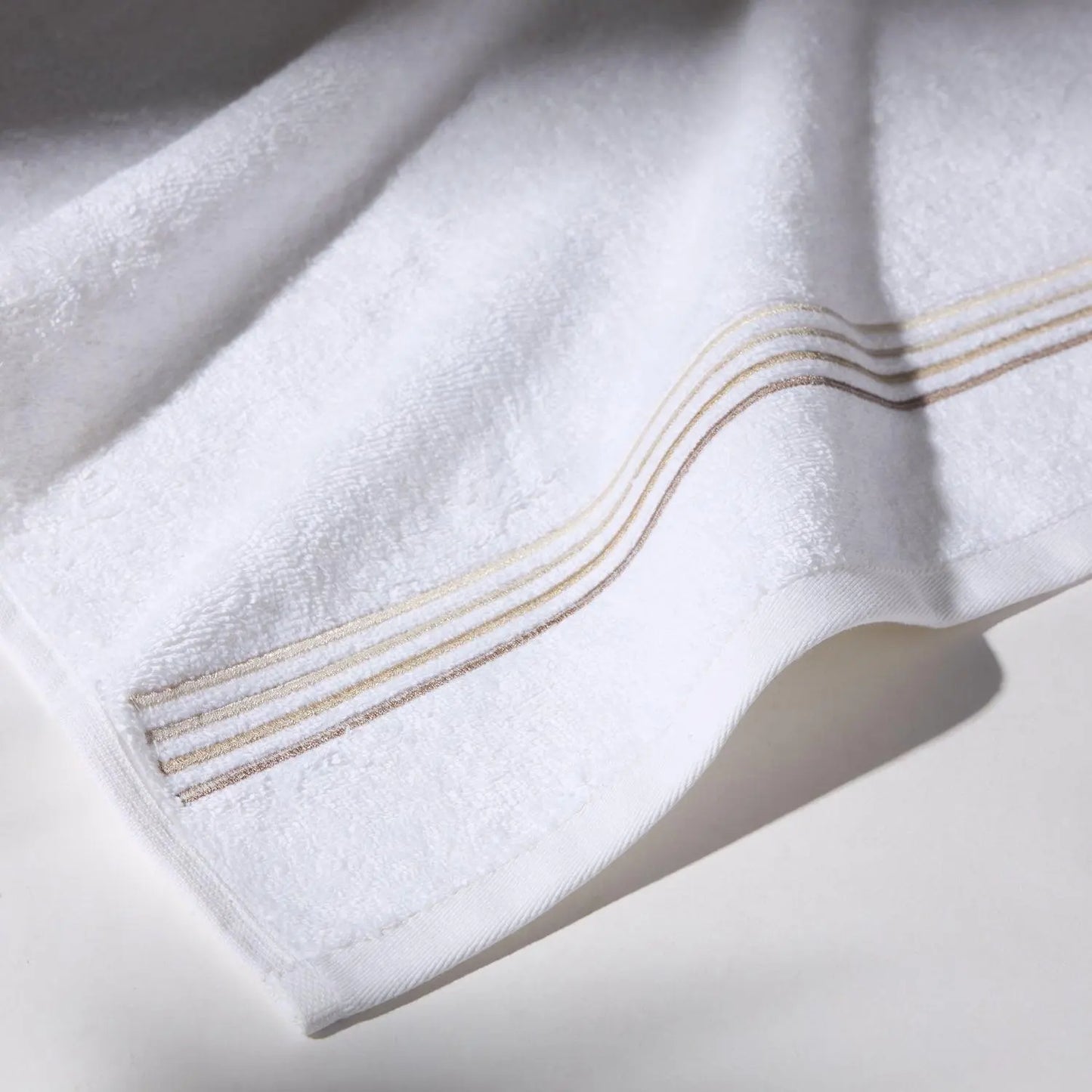 Detailed image of the stitching of a beige towel on a white surface, conveying a feeling of cleanliness and care for hygiene.