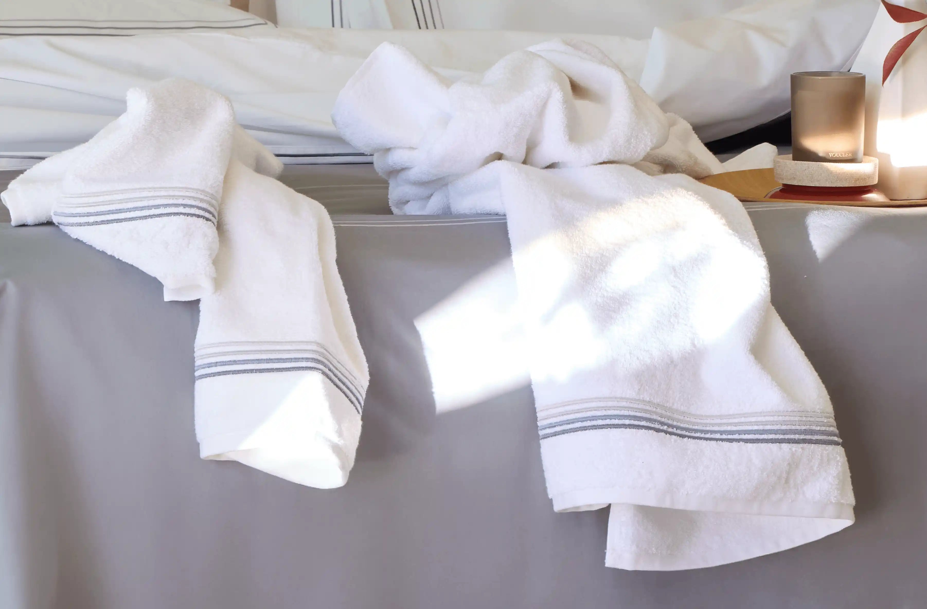Gray towels on the bed, illuminated by natural sunlight, create a calm and comfortable atmosphere in the room.