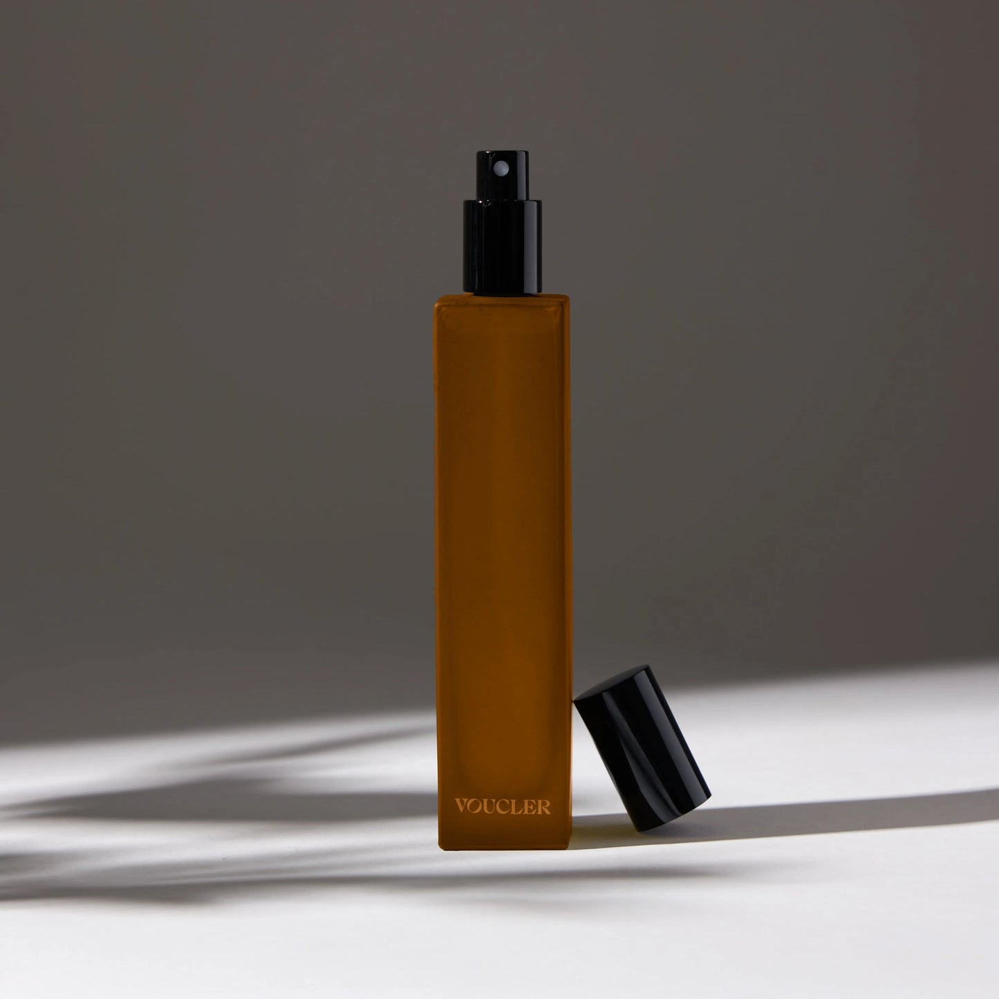 Voucler room spray bottle in amber with a black cap, featuring minimalist packaging on a neutral background, ideal for beauty and personal care.