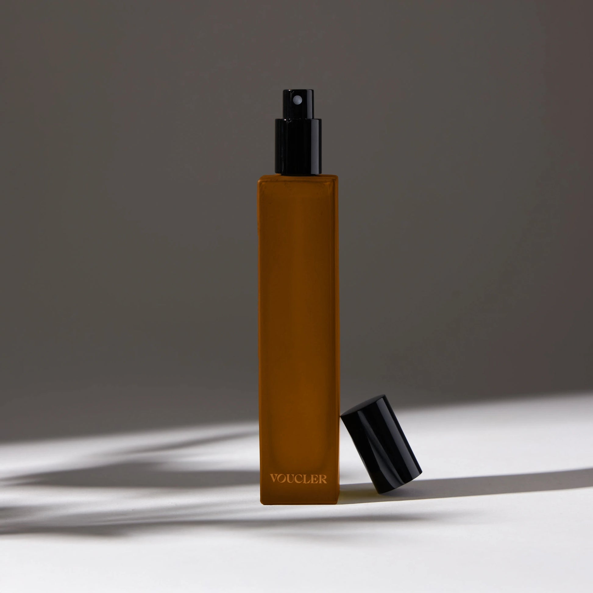 Voucler room spray bottle in amber with a black cap, featuring minimalist packaging on a neutral background, ideal for beauty and personal care.