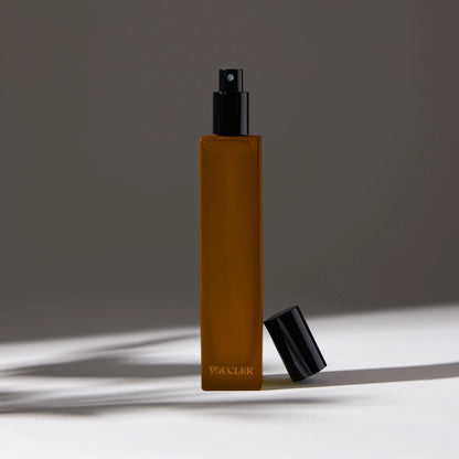 Voucler room spray bottle in amber with a black cap, featuring minimalist packaging on a neutral background, ideal for beauty and personal care.