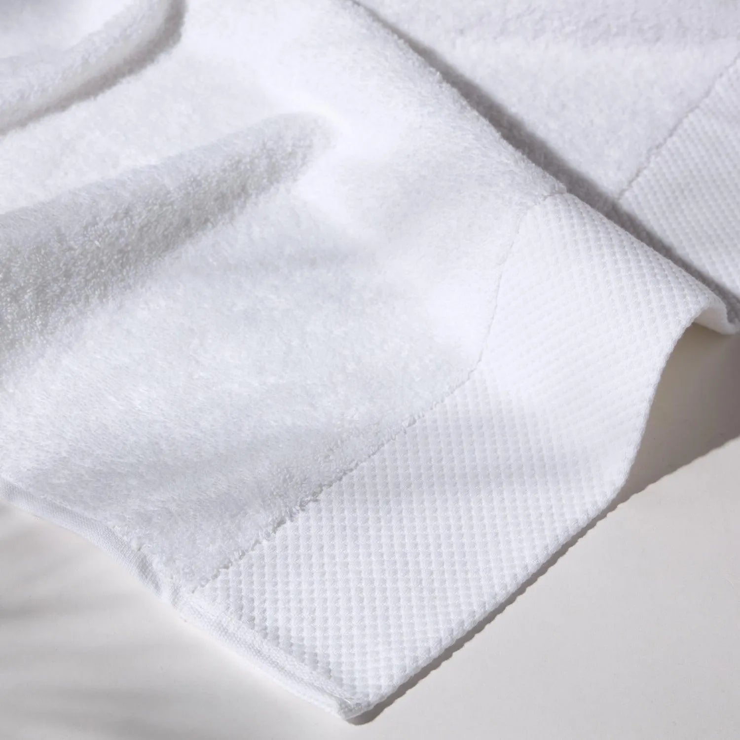 Detailed image of the stitching of a white towel on a white surface, conveying a feeling of cleanliness and care for hygiene.