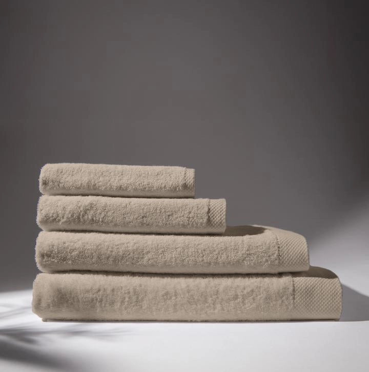 Image of four beige towels stacked on top of each other, with a soft gray background, conveying a feeling of cleanliness and care for hygiene.