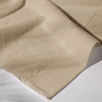Detailed image of the stitching of a beige towel on a white surface, conveying a feeling of cleanliness and care for hygiene.