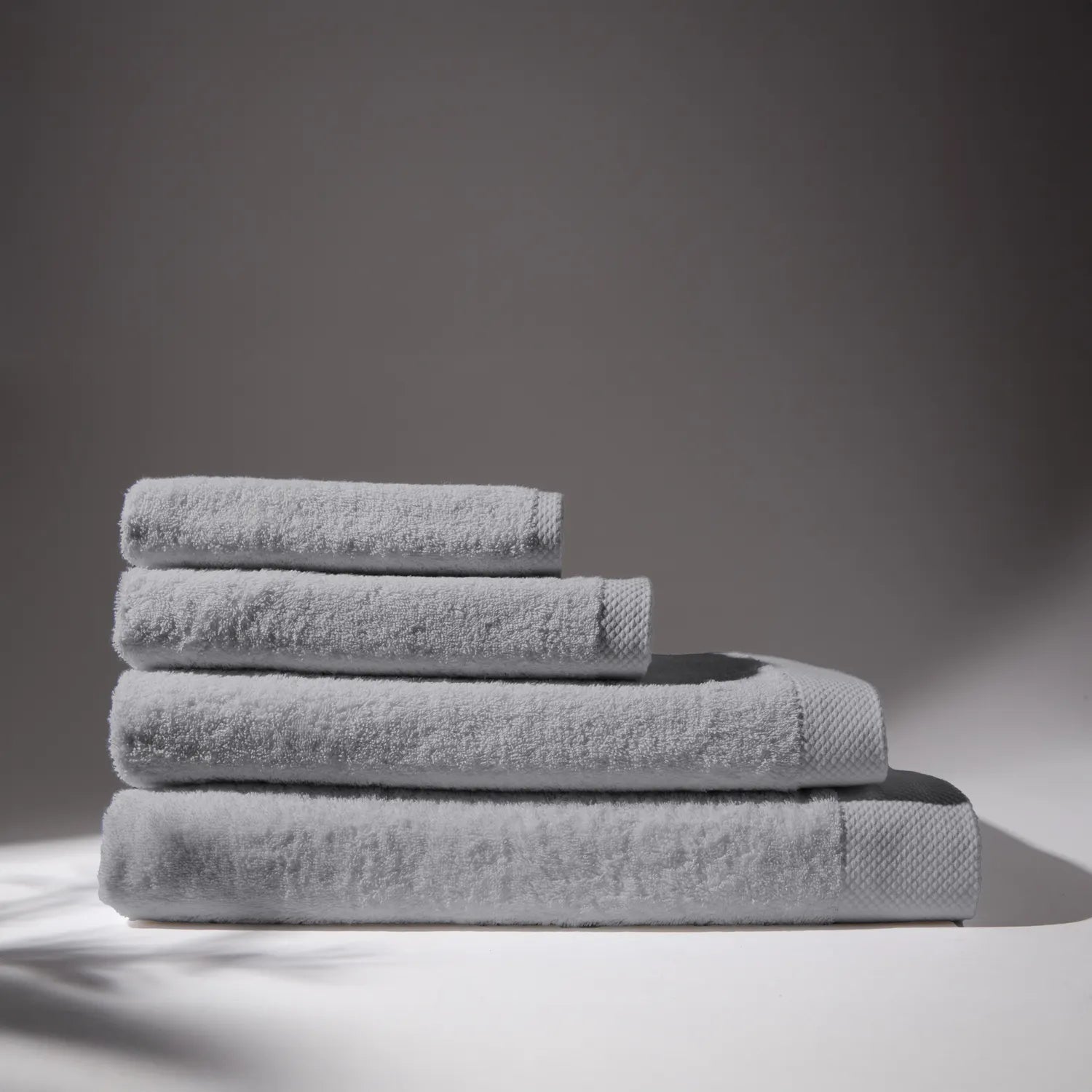 Image of four gray towels stacked on top of each other, with a soft gray background, conveying a feeling of cleanliness and care for hygiene.