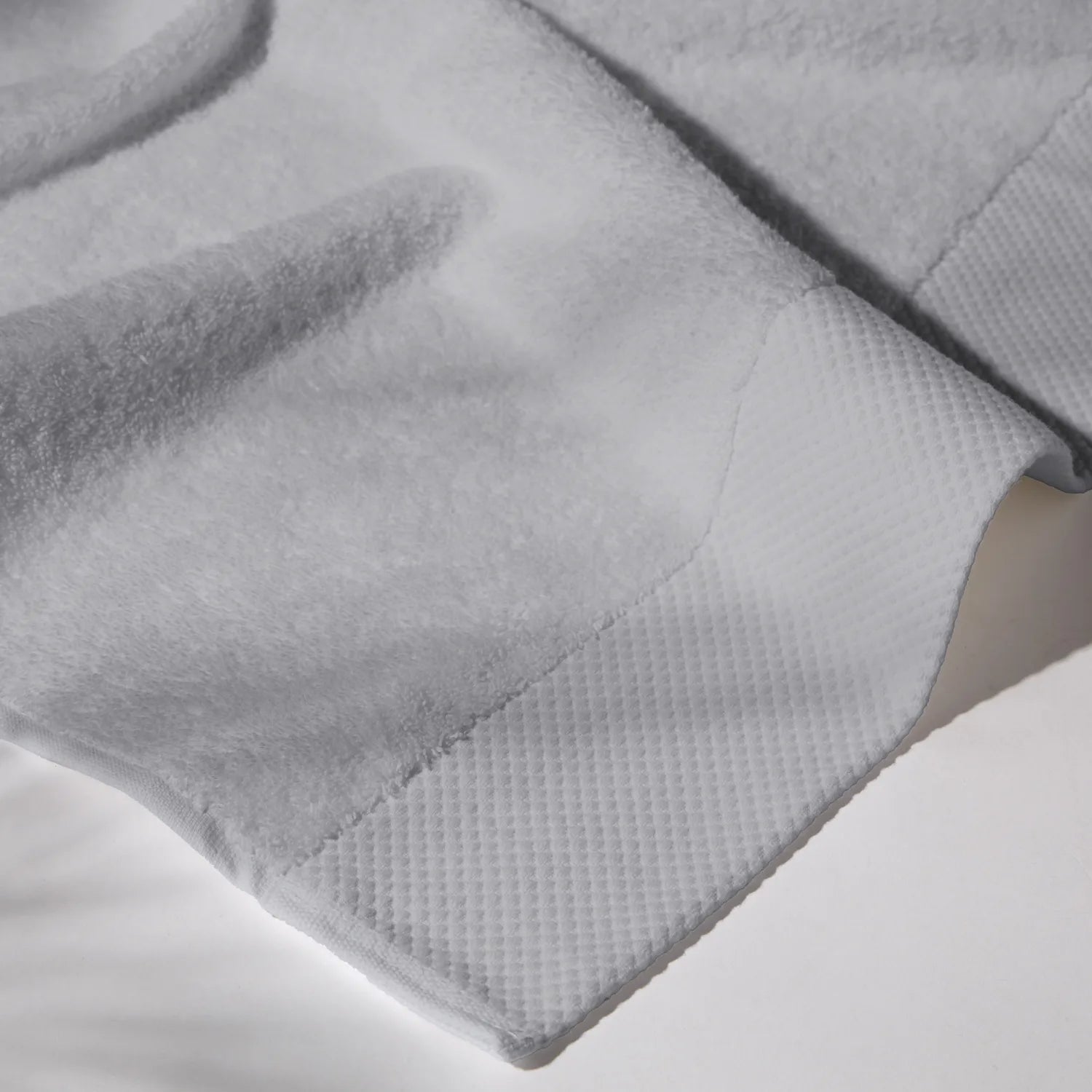 Detailed image of the stitching of a gray towel on a white surface, conveying a feeling of cleanliness and care for hygiene.