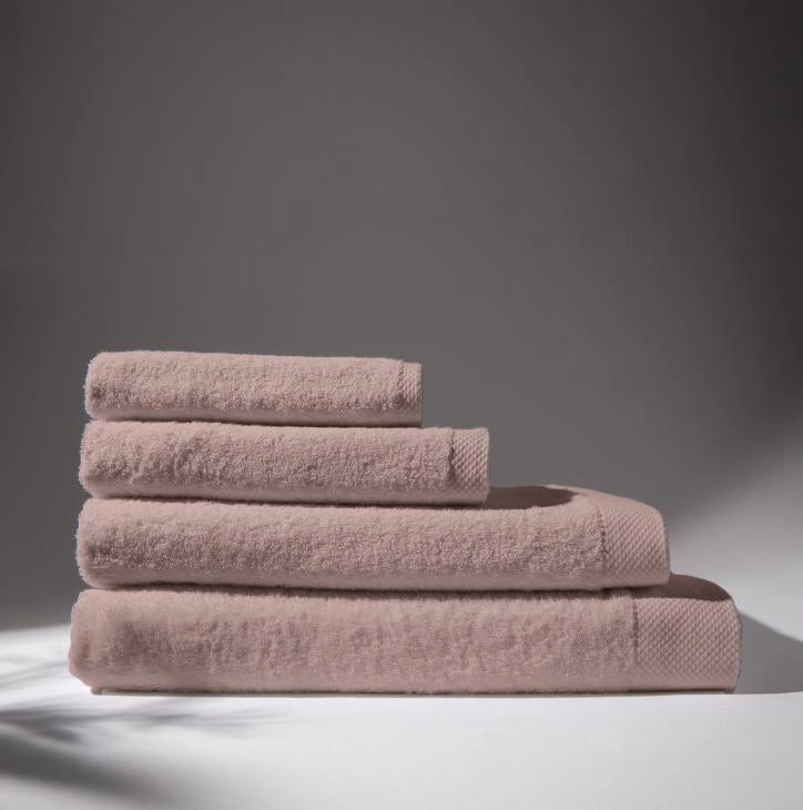 Image of four rose towels stacked on top of each other, with a soft gray background, conveying a feeling of cleanliness and care for hygiene.