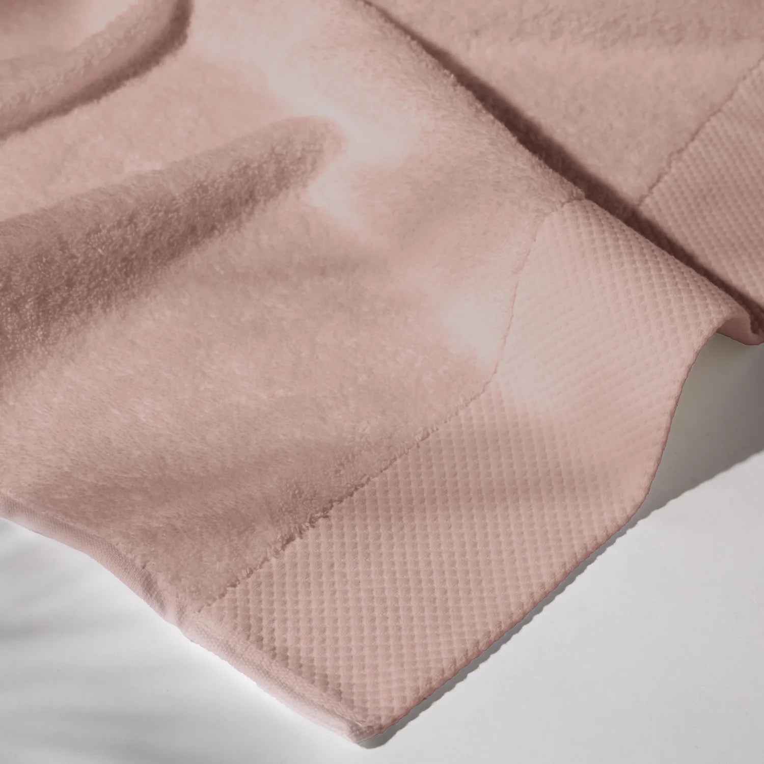 Detailed image of the stitching of a rose towel on a white surface, conveying a feeling of cleanliness and care for hygiene.