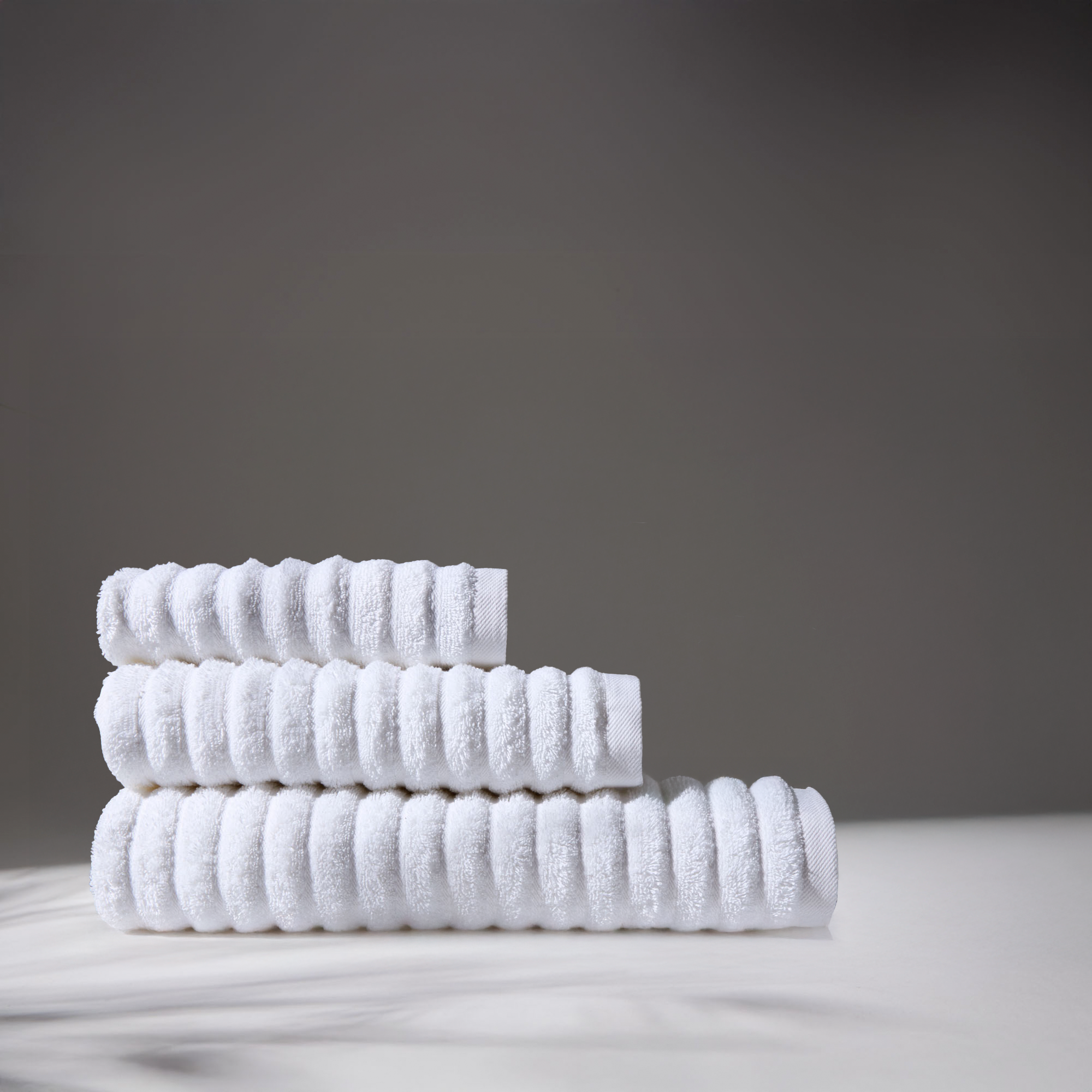 White towels stacked in different sizes on a white surface, with a gray background, conveying cleanliness and hygiene.