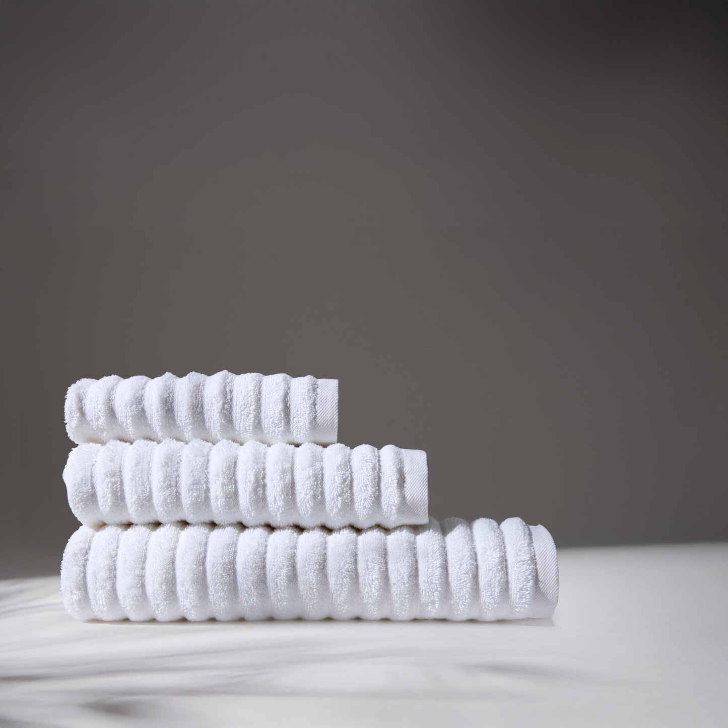 White towels stacked in different sizes on a white surface, with a gray background, conveying cleanliness and hygiene.