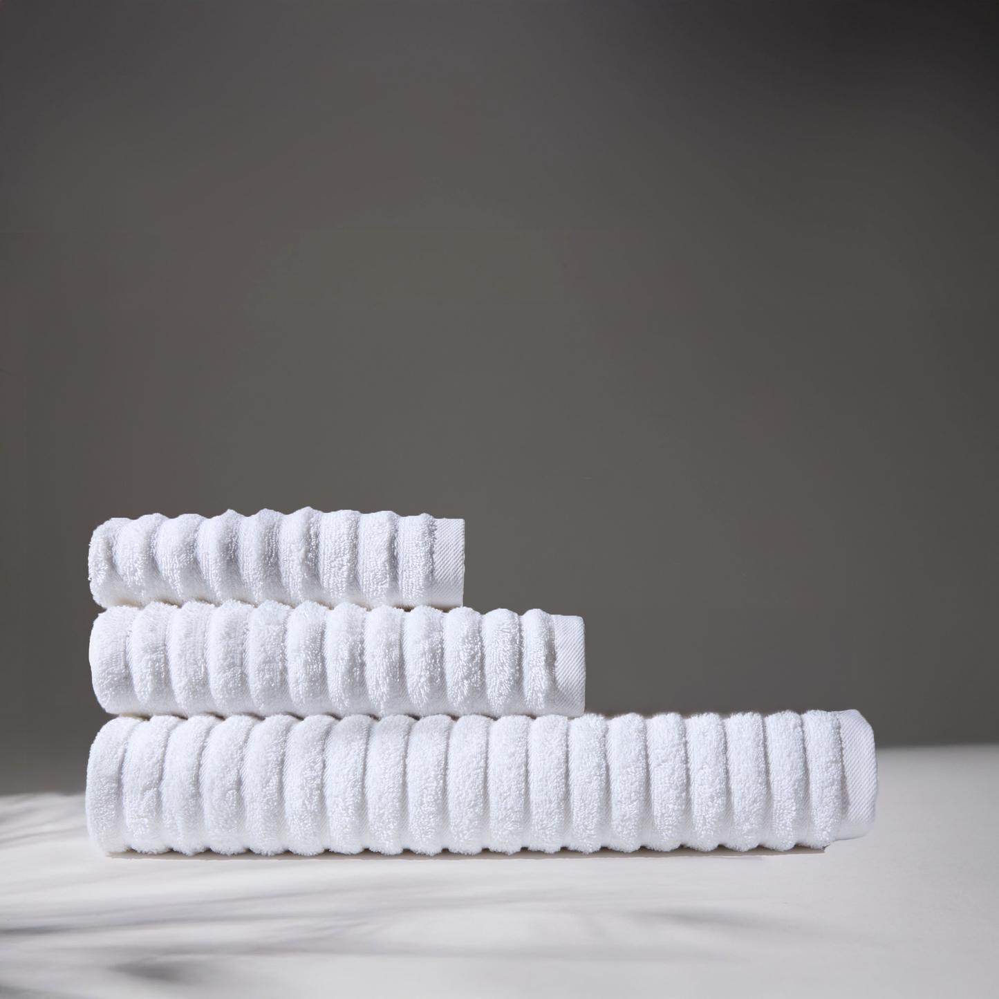 Image of three white towels stacked on a surface. The environment has a neutral background, conveying a sense of comfort and cleanliness.