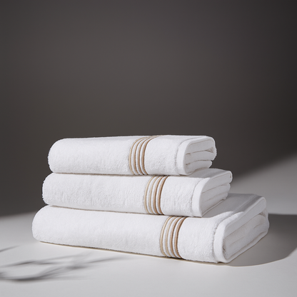 A set of folded white towels in a stack, with beige striped details, in an elegant and minimalist setting.