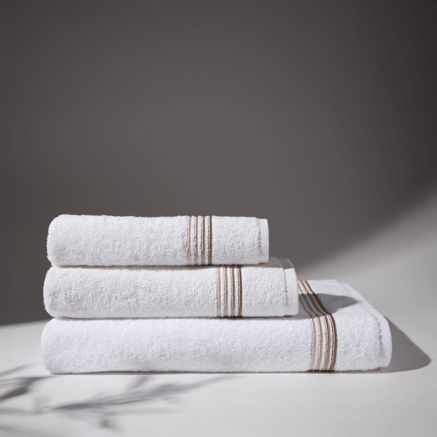 Set of white towels with beige stripes stacked under soft lighting, on a flat surface and neutral background.