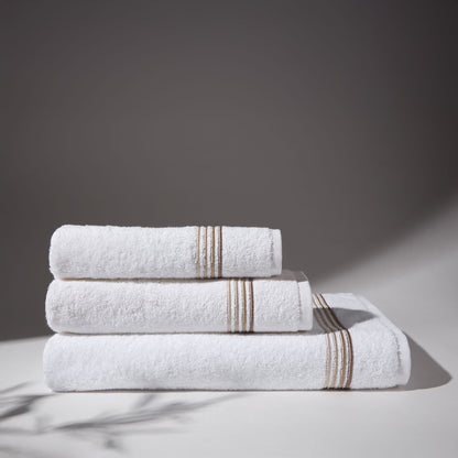 Set of white towels with beige stripes stacked under soft lighting, on a flat surface and neutral background.