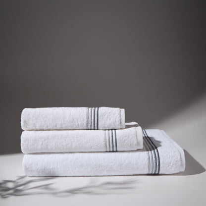 Set of three white towels with gray stripes folded on a surface with a gray background.