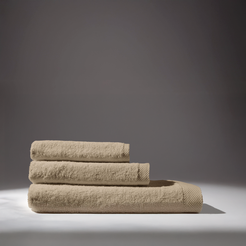 Three beige bath towels stacked on a white surface with a dark gray background.