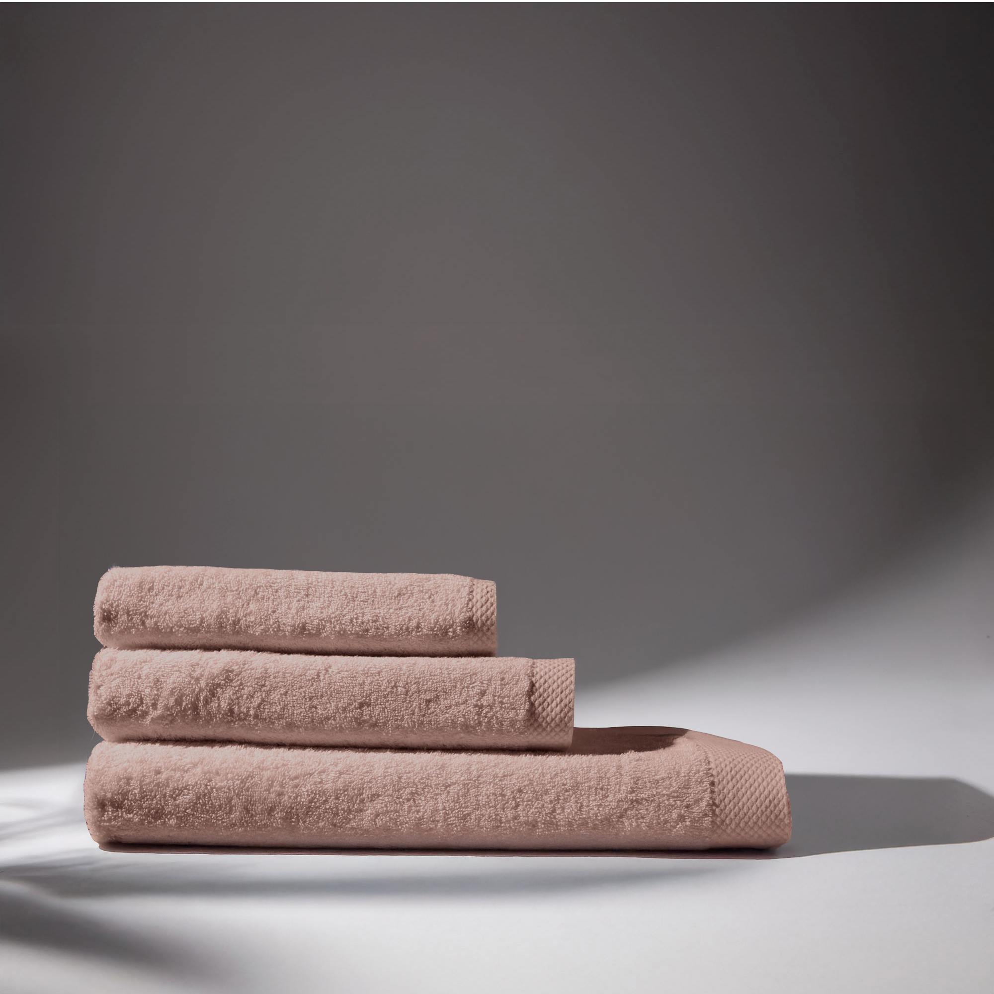Set of three rose bath towels, folded and stacked on a white surface with light background.