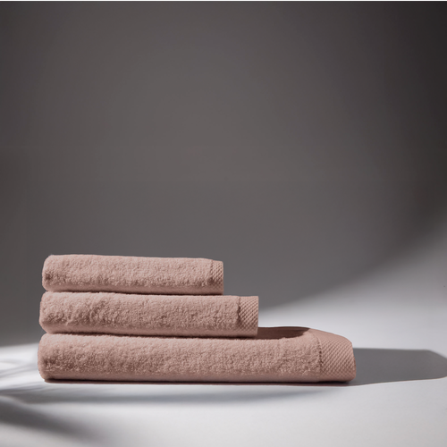 Set of three rose bath towels, folded and stacked on a white surface with light background.