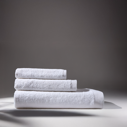 Three folded white towels stacked on a surface, with a soft gray background, creating an atmosphere of cleanliness and elegance.