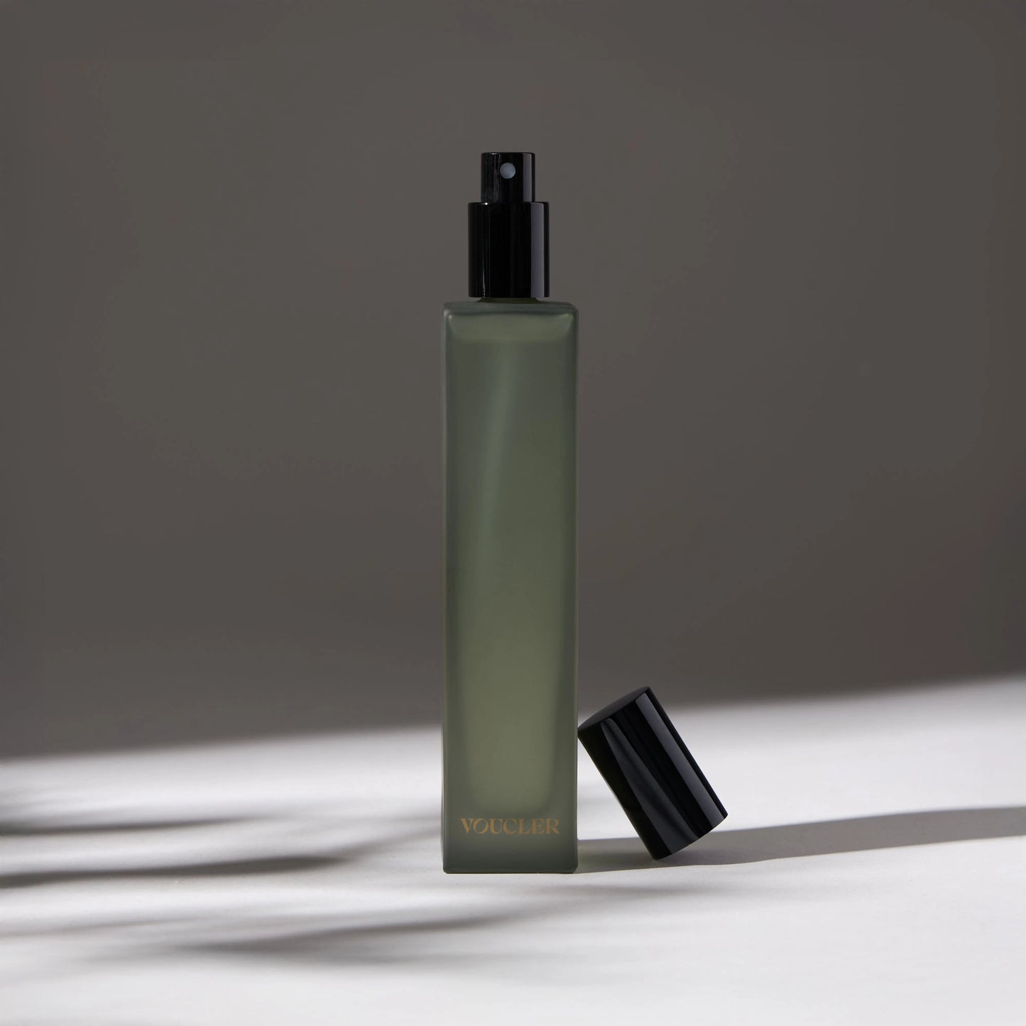 Voucler room spray bottle in green with a black cap next to the bottle, highlighting the minimalist packaging on a neutral background.